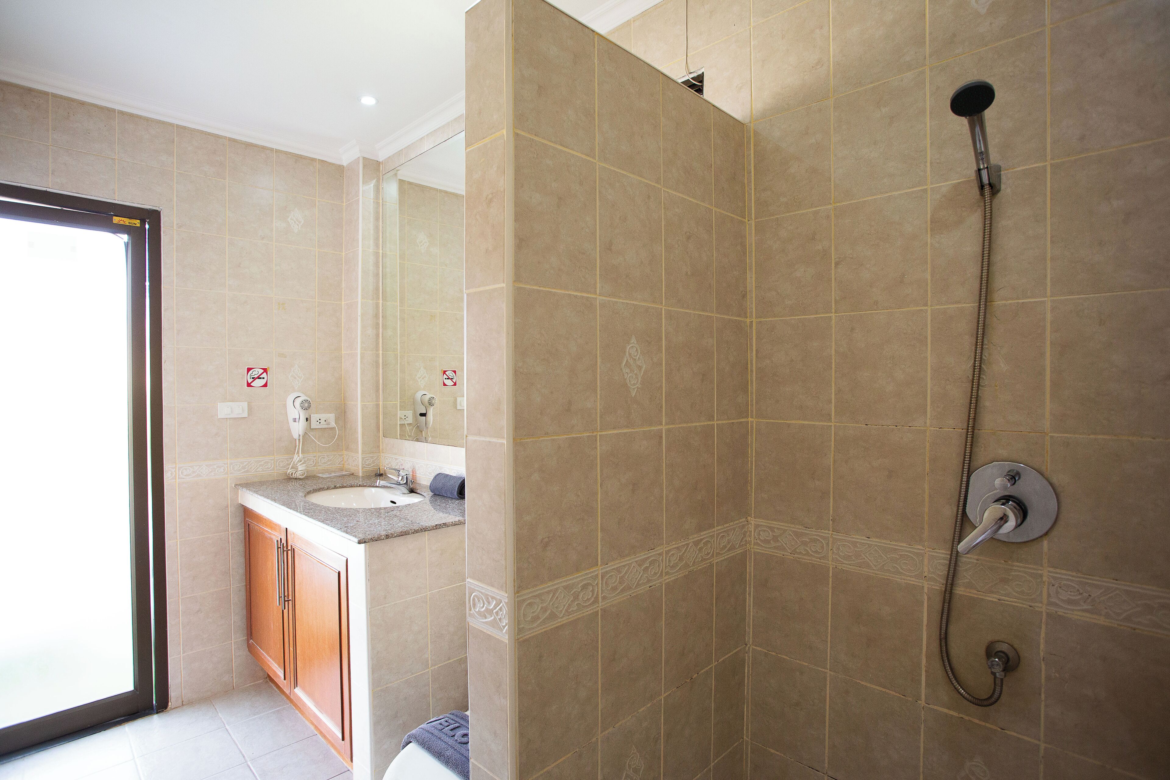 A bathroom with beige tiles, a shower with a handheld showerhead, a sink with a mirror, and wooden cabinets.