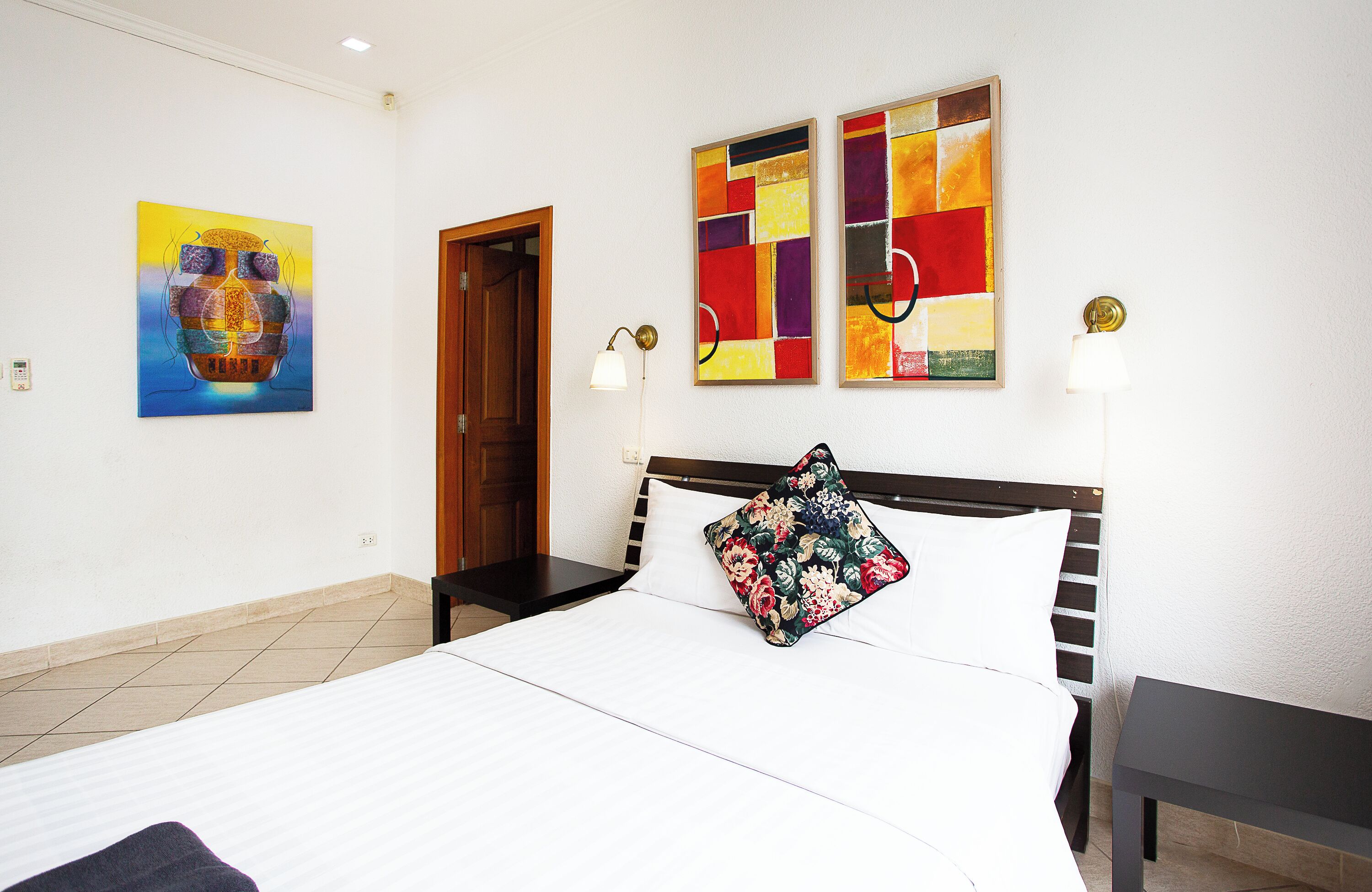 A hotel room with a large bed, a wooden headboard, two wall-mounted lamps, and two abstract paintings.