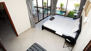 A hotel room with a bed, a small table, and a view of a swimming pool and garden.