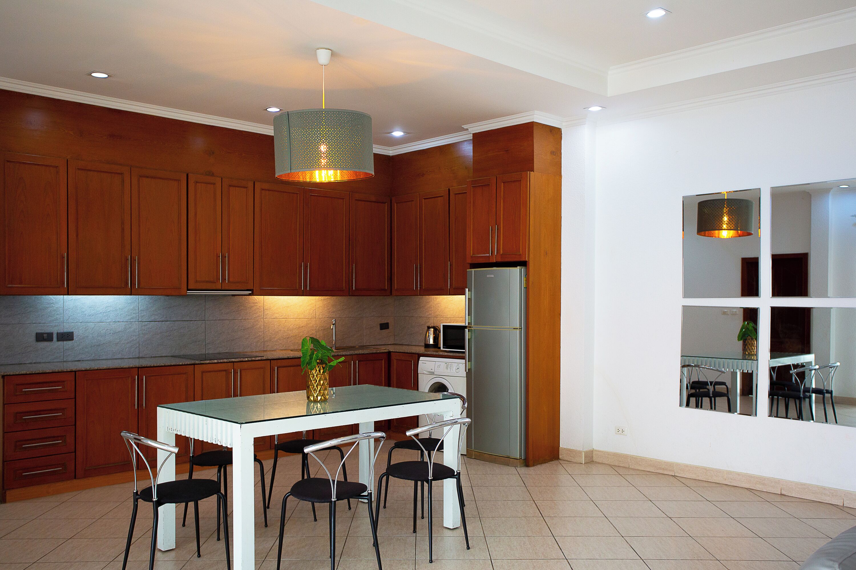 Una cocina moderna con armarios de madera, un refrigerador de acero inoxidable, una mesa de comedor con cuatro sillas e iluminación colgante.