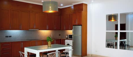 Una cocina moderna con armarios de madera, un refrigerador de acero inoxidable, una mesa de comedor con cuatro sillas e iluminación colgante.