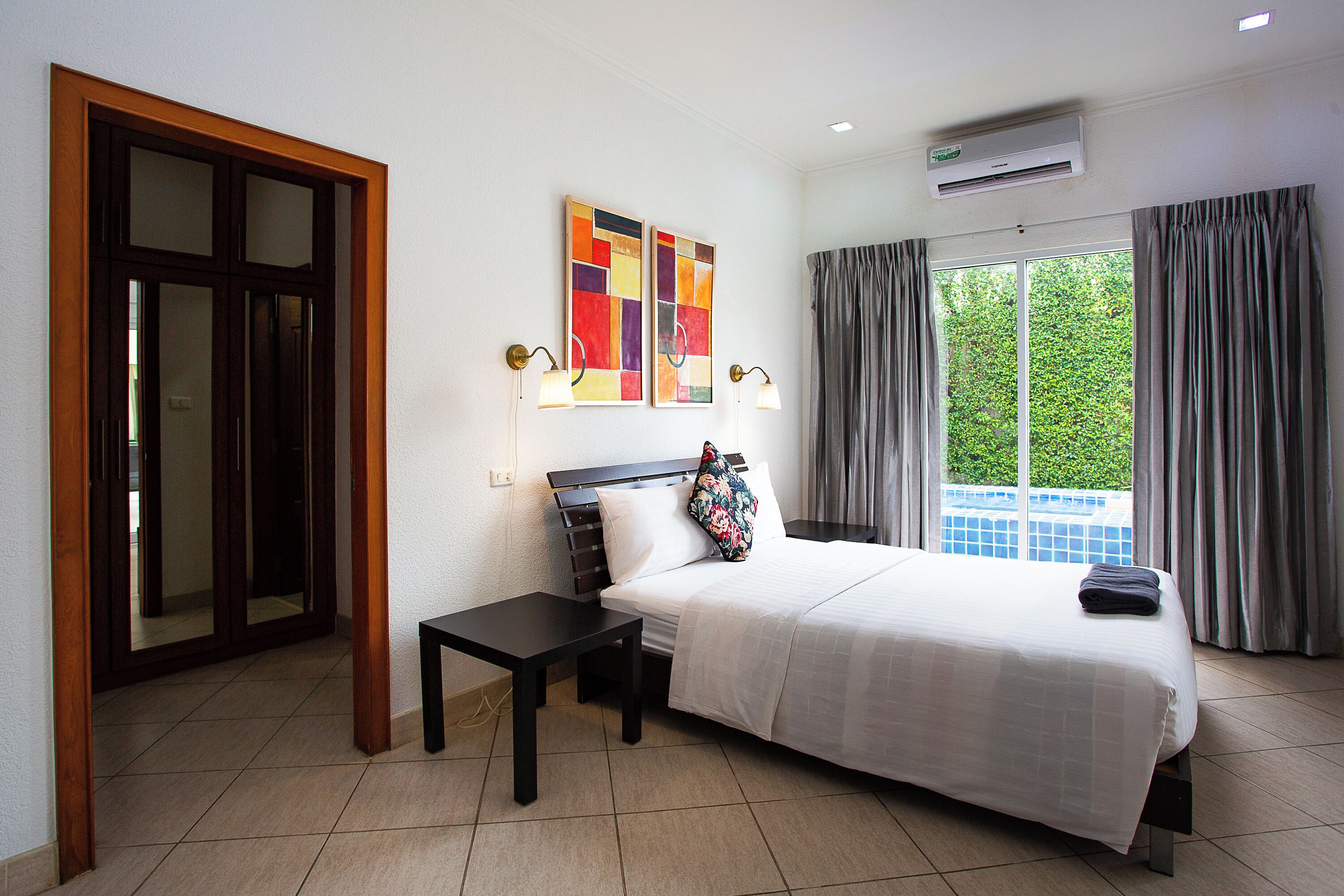 A hotel room with a bed, a nightstand, a window with curtains, and artwork on the wall.