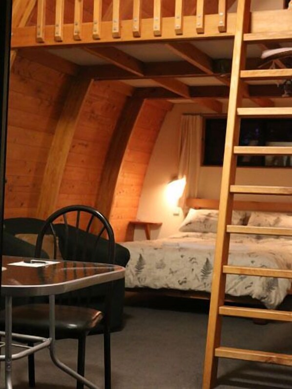 A cozy attic room with a bunk bed, a small table with chairs, and a ladder. - Wetland View Park (Mangarakau)