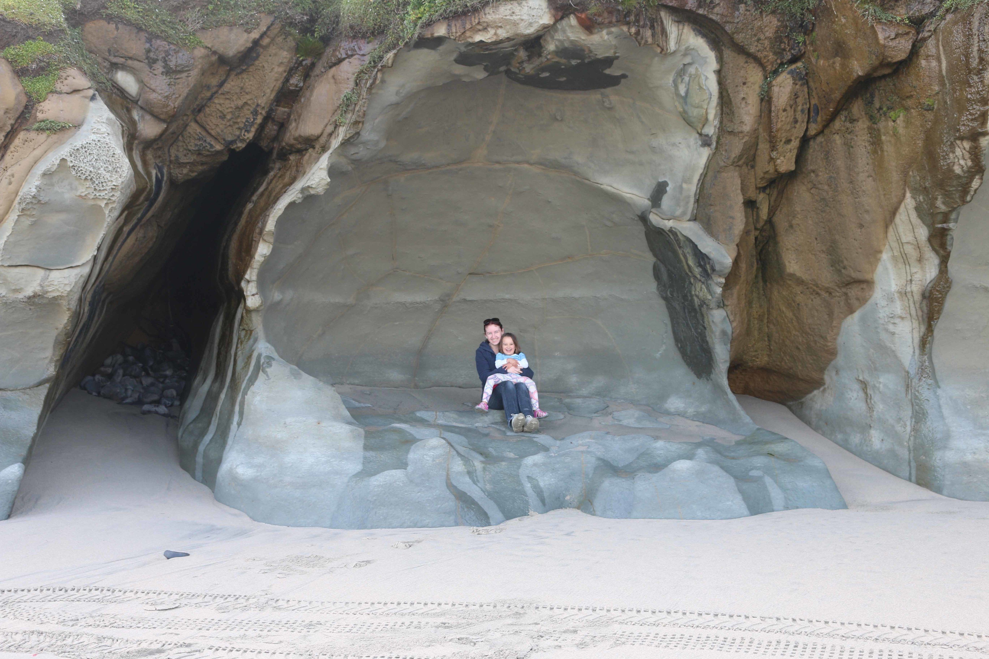 A couple sitting in a cave-like structure with a sandy floor and rocky walls.