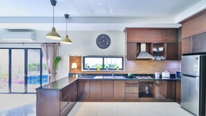 A modern kitchen with a central island, dark wooden cabinets, a stainless steel refrigerator, and a large window with a view of greenery outside. - Sweet Villa Pattaya (Pattaya)