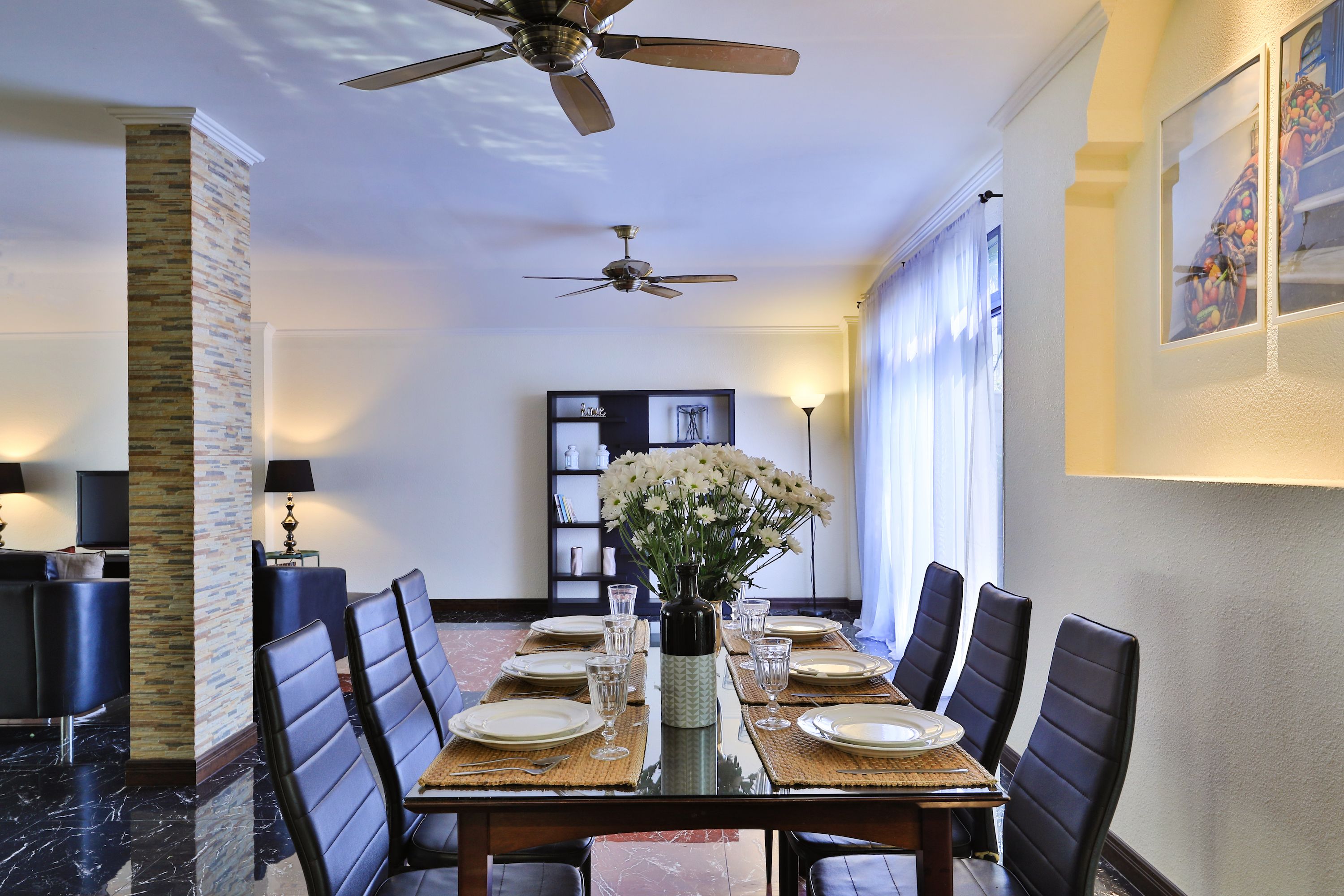 A dining area with a table set for four, a vase of flowers, and ceiling fans.