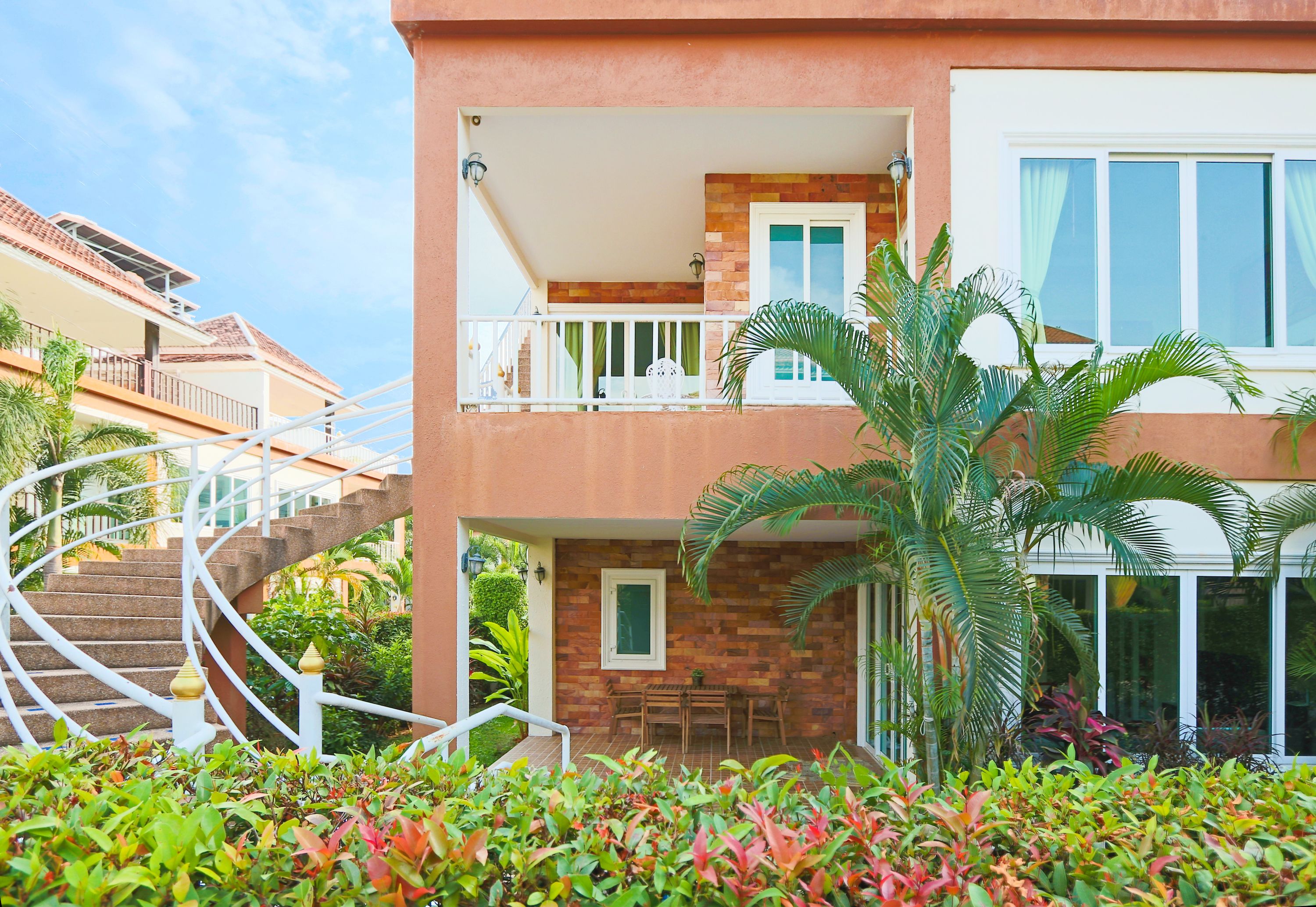 A two-story building with a balcony, a staircase, and a garden area with various plants.