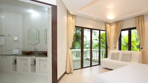 A hotel room with a large bed, a sitting area with a sofa, a bathroom with a glass-enclosed sink, and a balcony with a view of greenery. - Sweet Villa Pattaya (Pattaya)