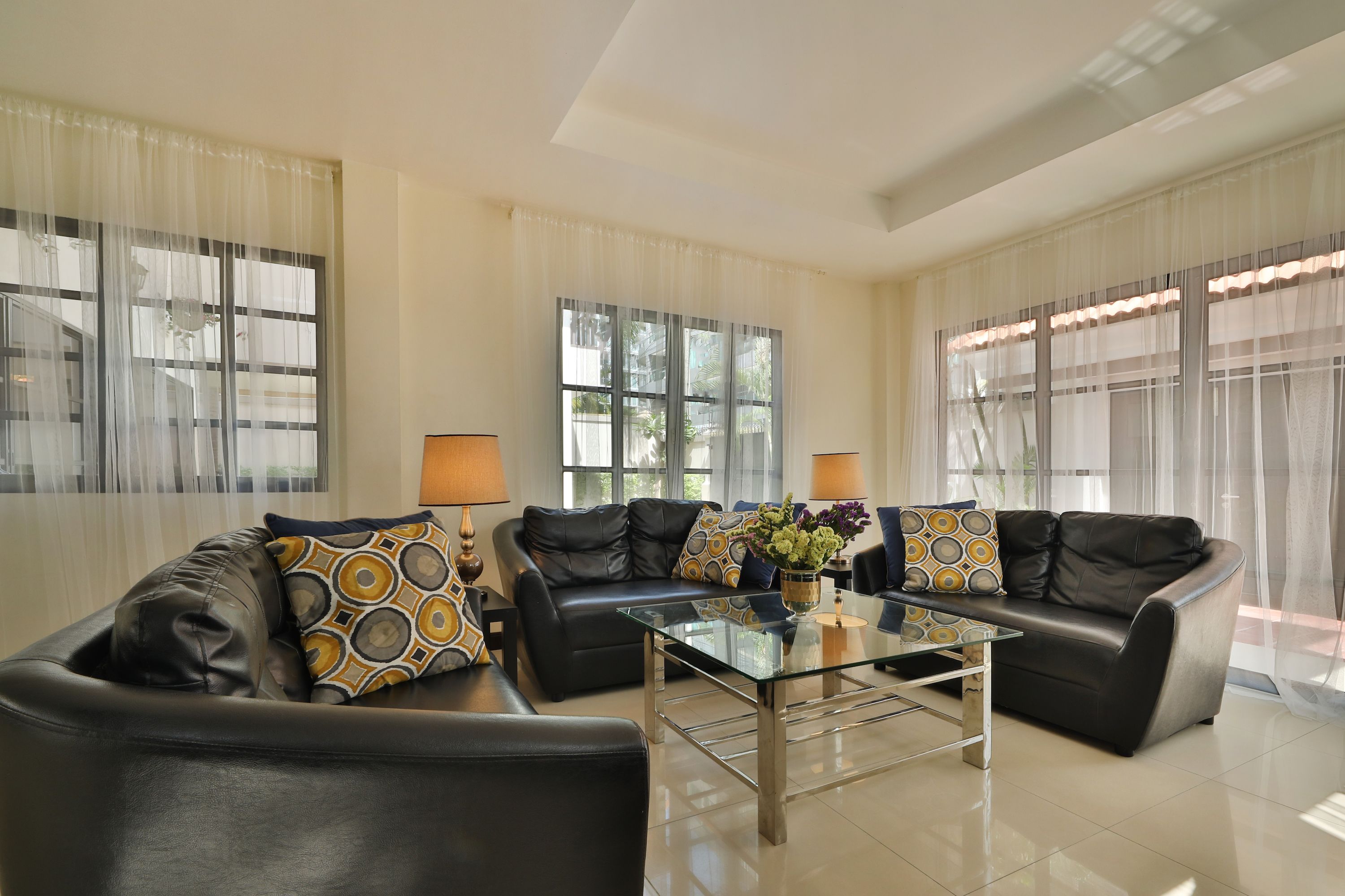 A modern living room with two black leather sofas, a glass coffee table, and a potted plant.