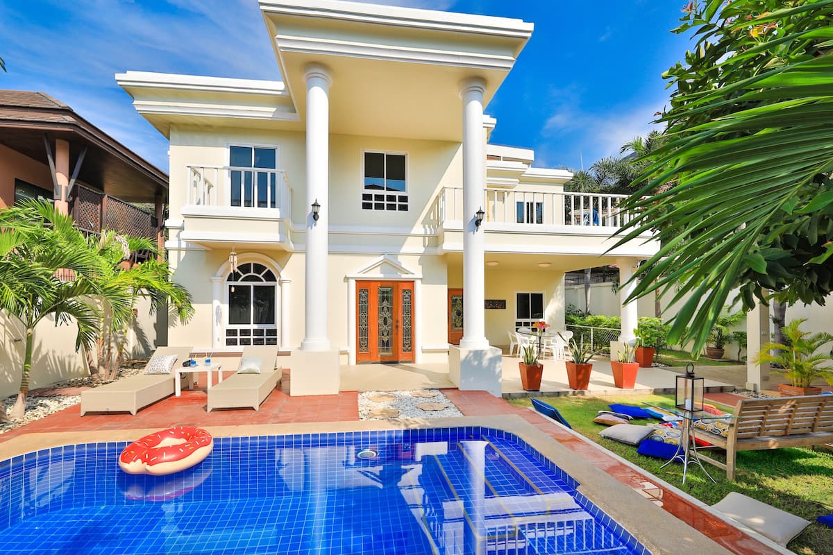 A large, two-story house with a swimming pool, outdoor furniture, and potted plants.