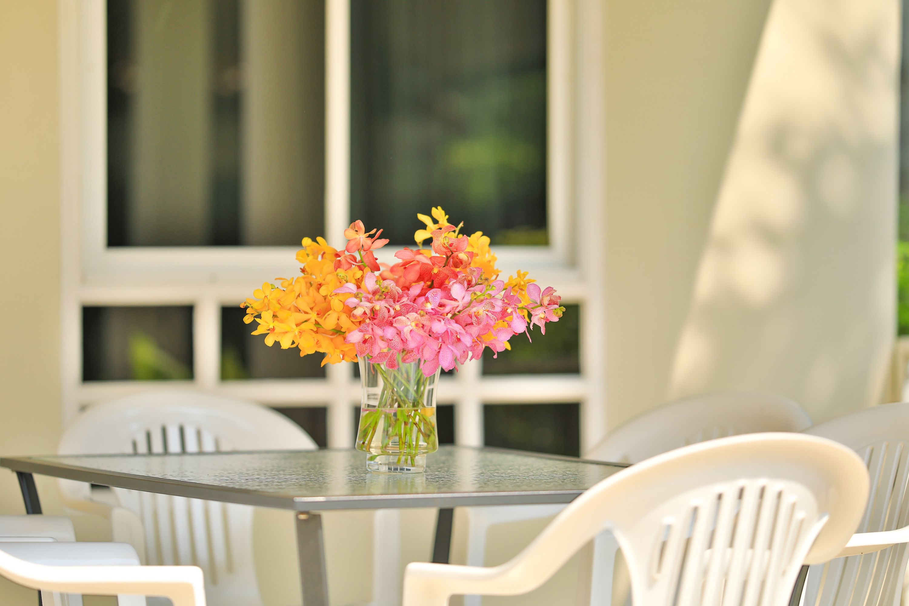 A table with a vase of flowers and white chairs.