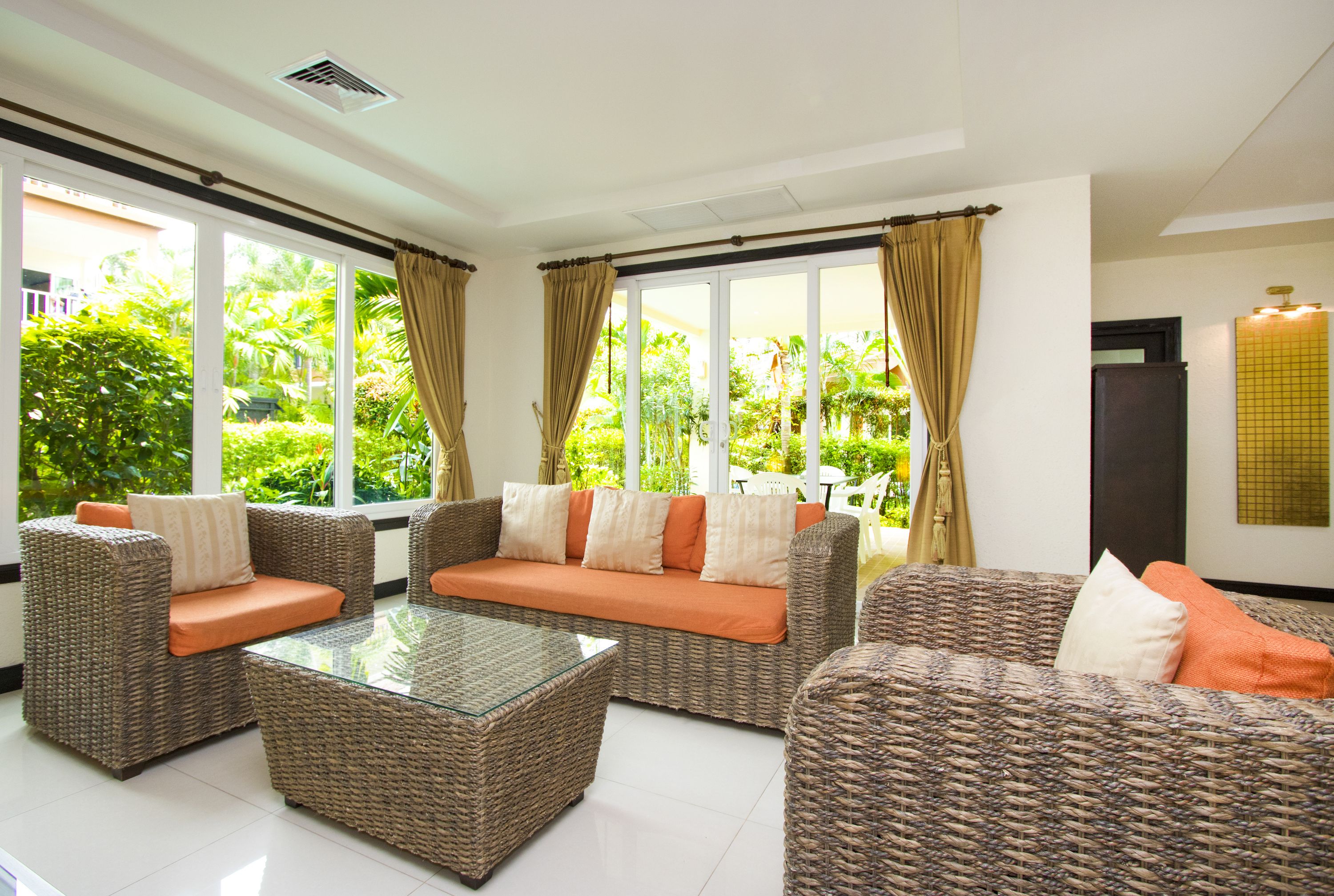 A spacious living area with wicker furniture, large windows, and a view of greenery outside.