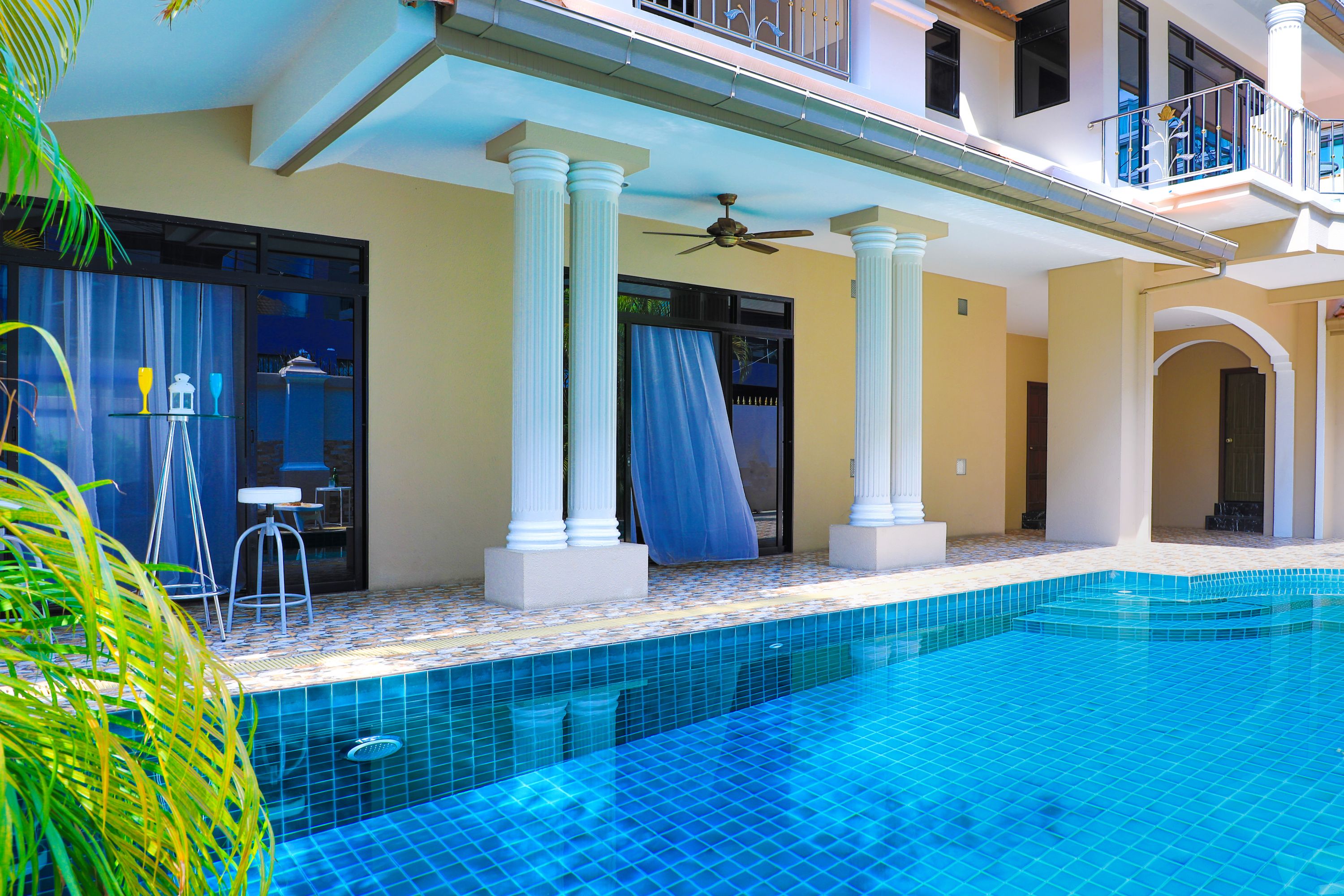A swimming pool with a tiled edge, a ceiling fan, and a balcony with a railing.
