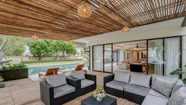 Un área exterior moderna para el esparcimiento, con mobiliario de mimbre, una terraza de madera y un ventanal que da a una piscina.