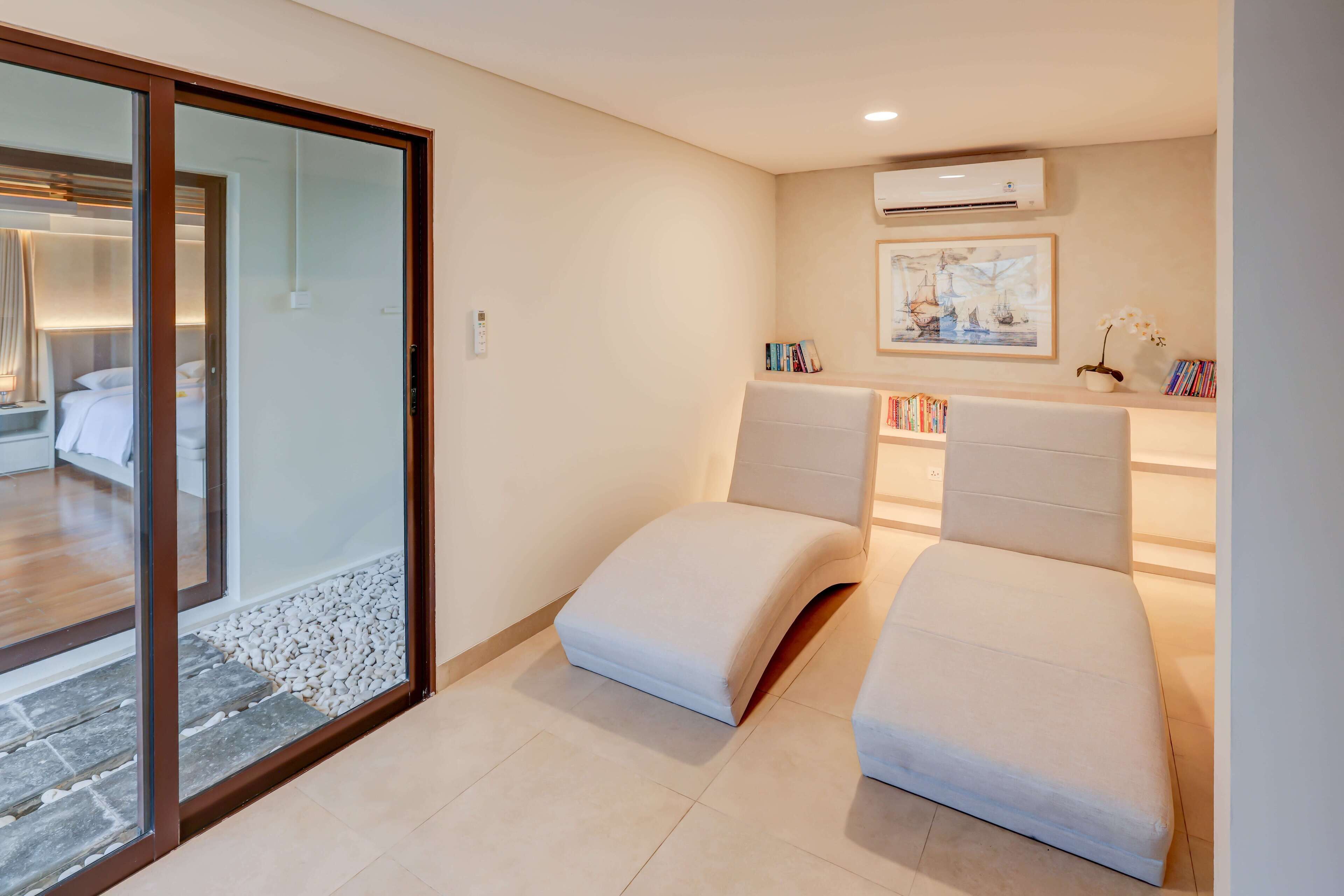 A modern hotel room with a glass door leading to a balcony, a sofa, a bedside table, and a wall-mounted air conditioner.