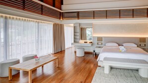 Una habitación de hotel moderna con piso de madera, una cama grande, un escritorio, una silla y un ventanal con cortinas.