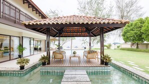 Un espacio exterior cubierto con piscina, terraza de madera y dos sillas de mimbre.