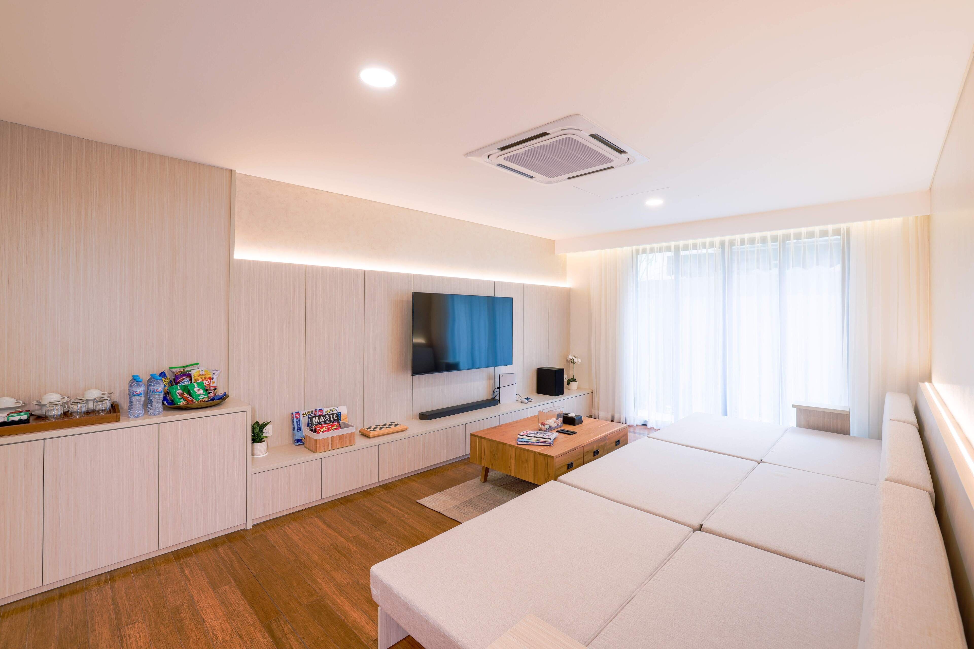 A modern hotel room with a sofa bed, a flat-screen TV, a wooden coffee table, and a small TV on a stand.