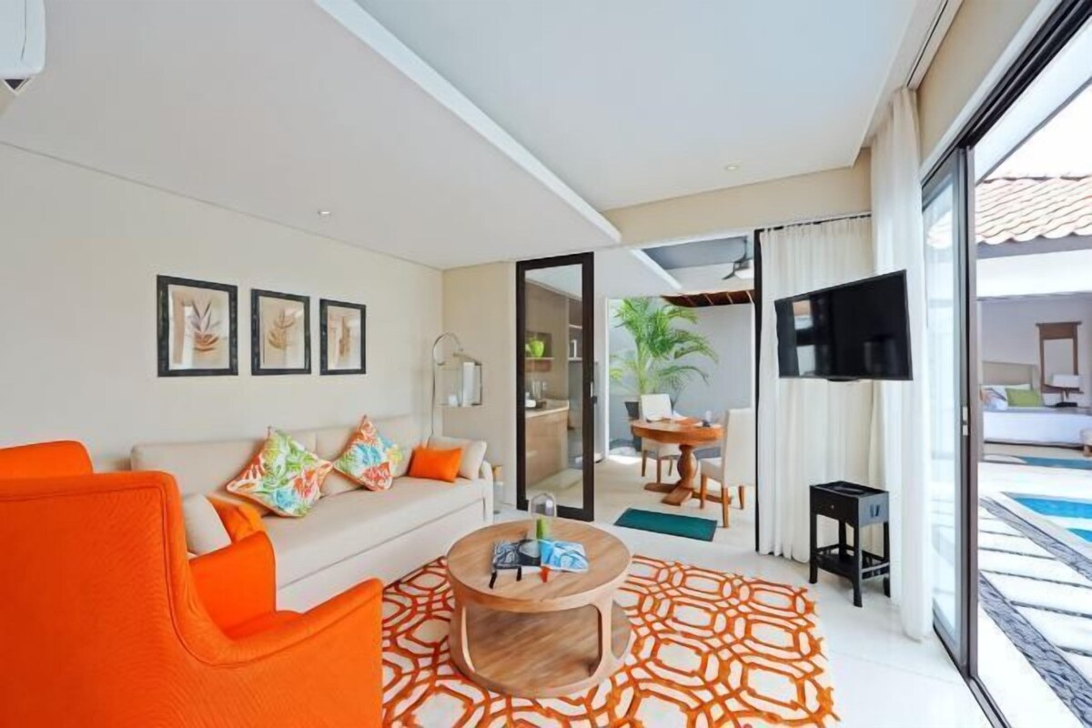 A modern living room with a sofa, coffee table, and a view of a pool through large glass doors.