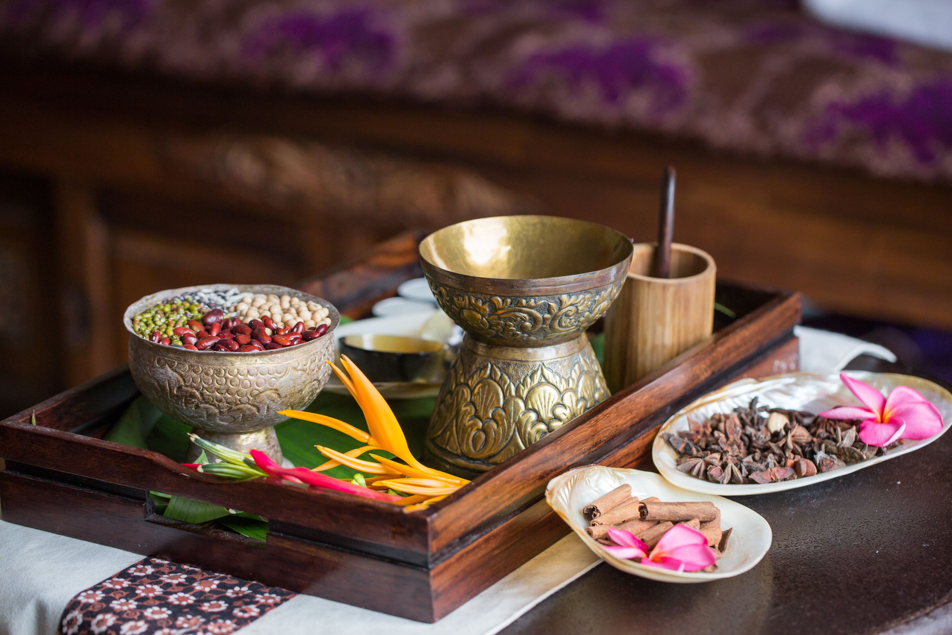A tray with various items including a bowl of beans, a brass container, and plates with spices and flowers.