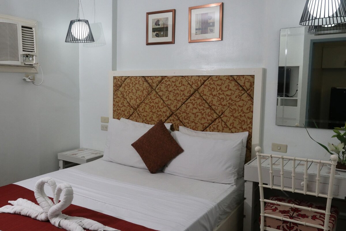 A hotel room with a bed, a bedside table, a mirror, and a wall-mounted air conditioner.