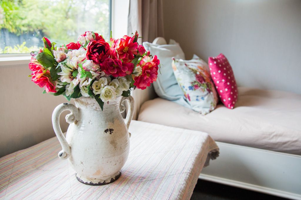 A white ceramic pitcher with a bouquet of red, pink, and white flowers on a table.