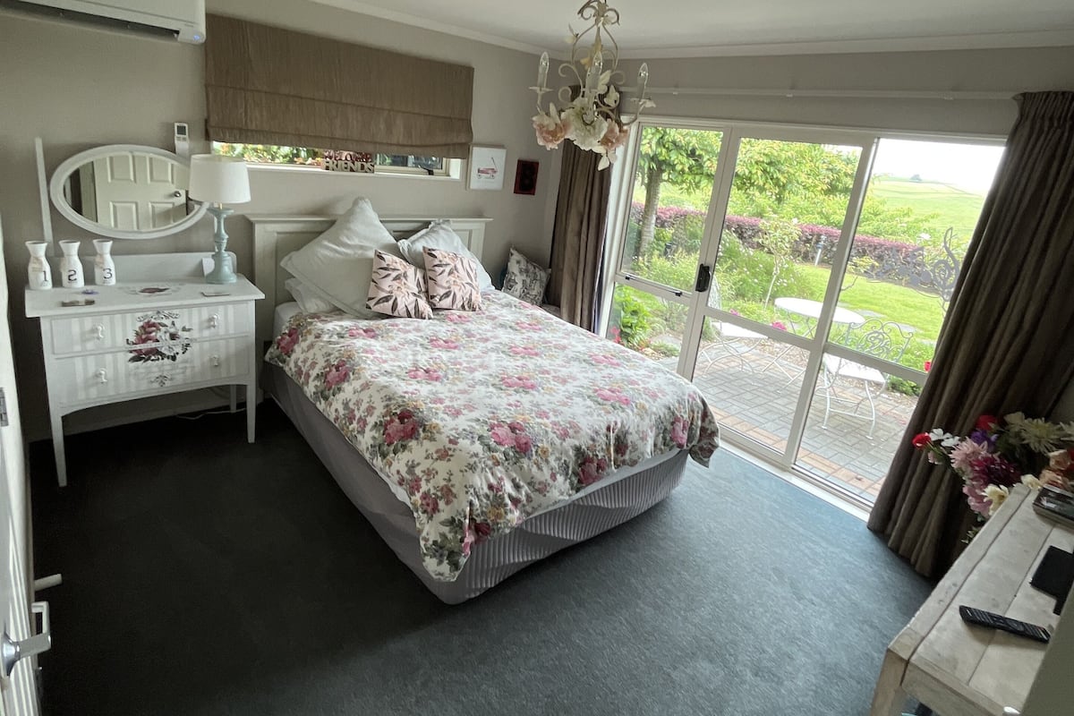 A bedroom with a bed, bedside table, dresser, and a view of the outdoors.