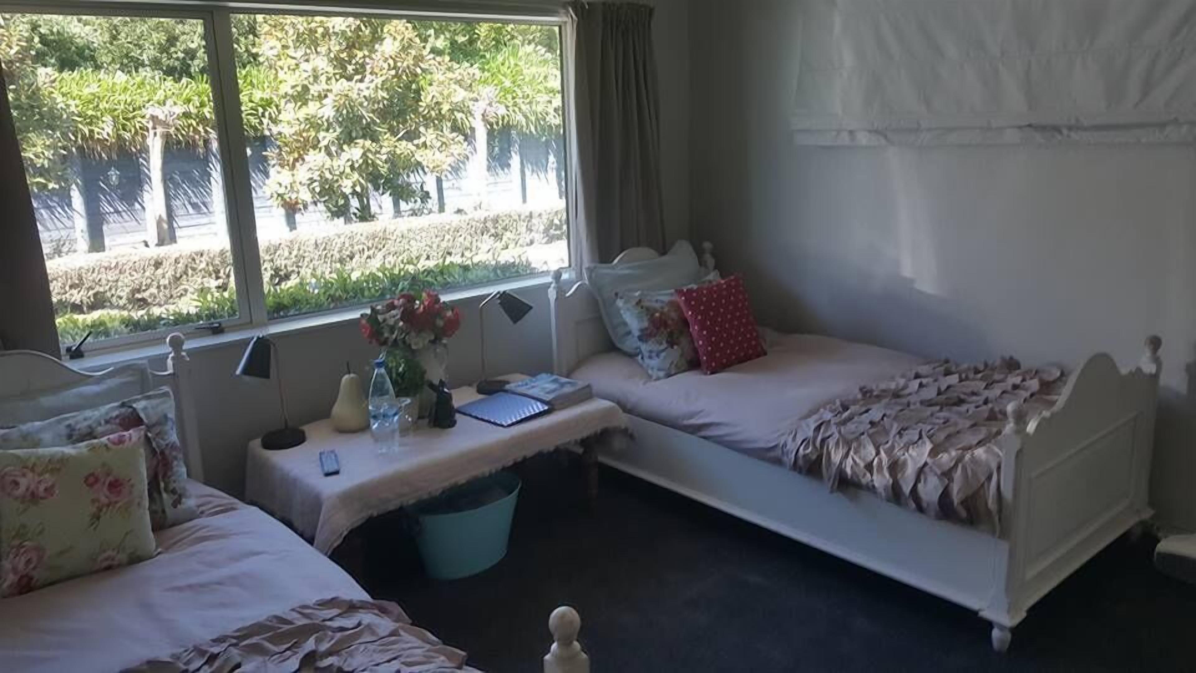 Un dormitorio con dos camas individuales, un escritorio pequeño y una ventana con vistas a árboles.