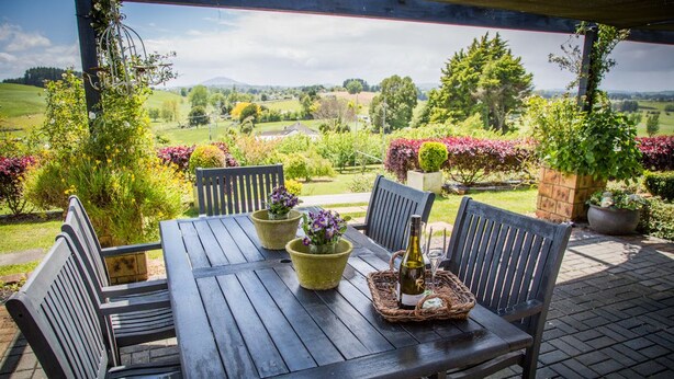 Une table en bois installée à l’extérieur, avec des chaises, des plantes en pot et une bouteille de vin.