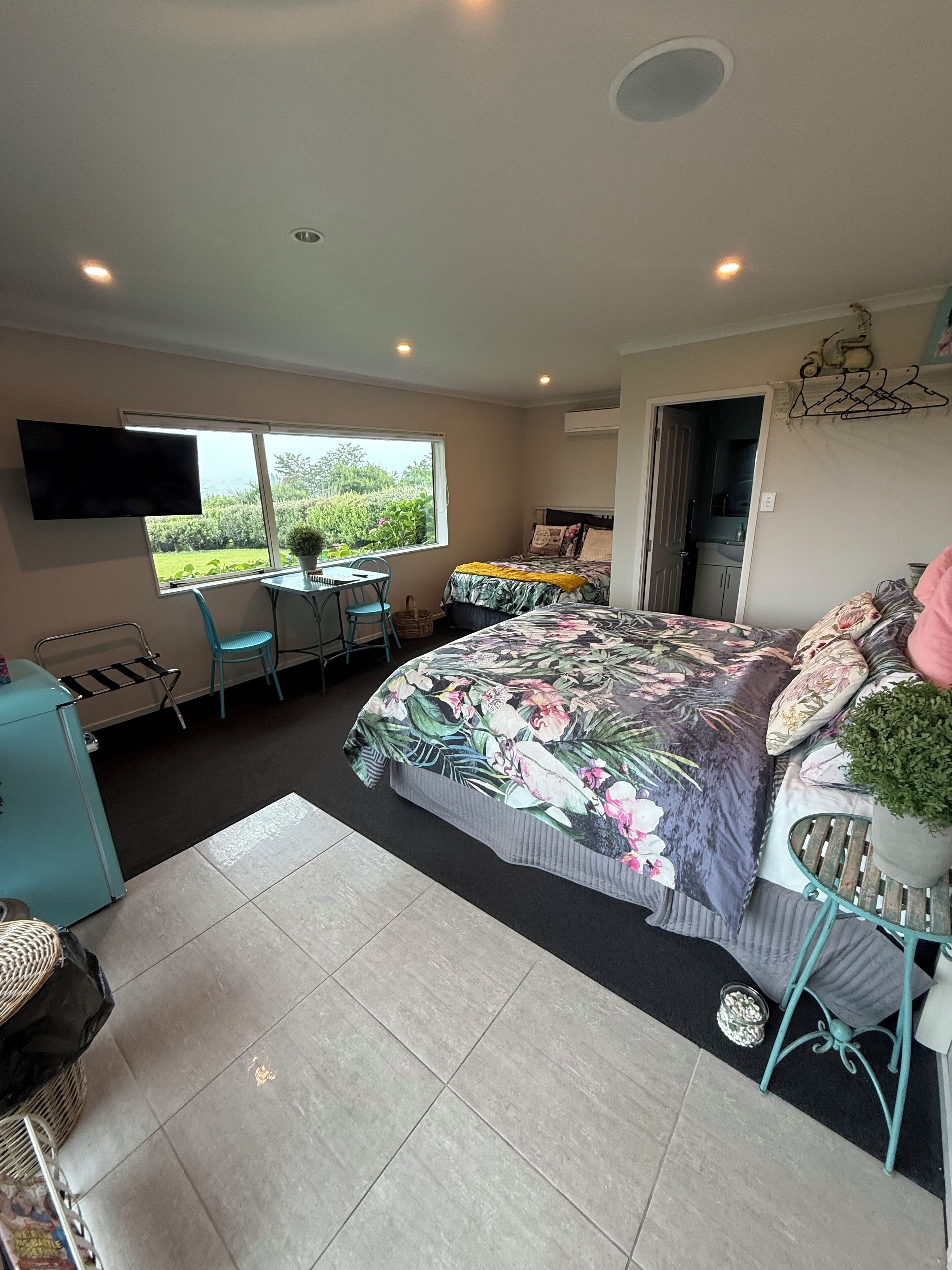 Un dormitorio con cama, escritorio y silla. Se ve un ventanal con vistas a la vegetación.