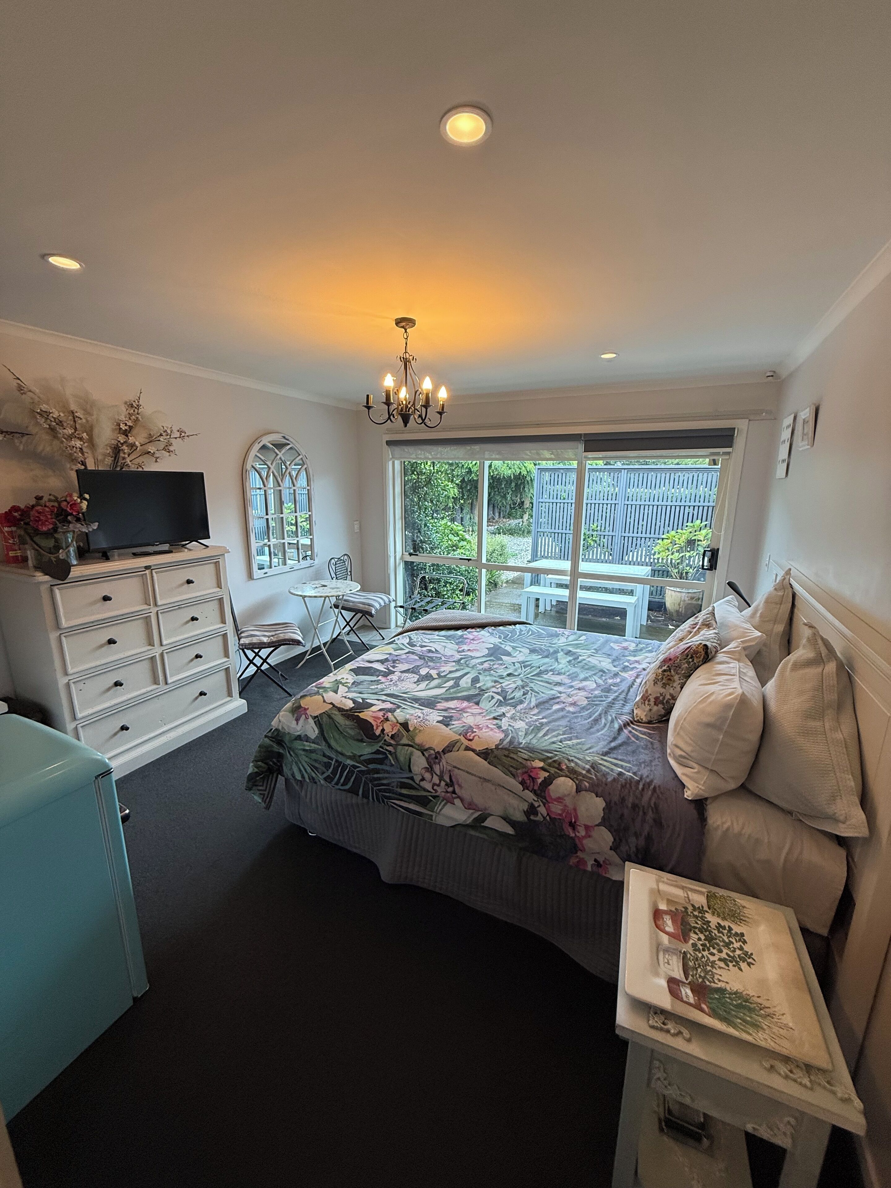 A bedroom with a bed, dresser, TV, and a window with a view of the outdoors.