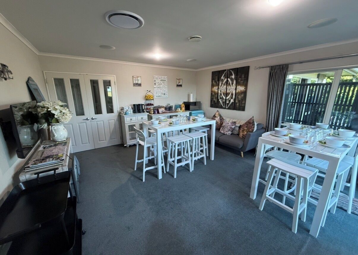 A spacious kitchen with white furniture, a dining area with white tables and chairs, and a grey carpeted floor.