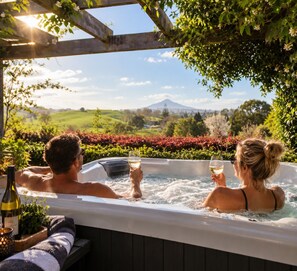 A hot tub with two people holding glasses, surrounded by greenery and a scenic view. - Waitomo Orchard Estate B&B (Otorohanga)