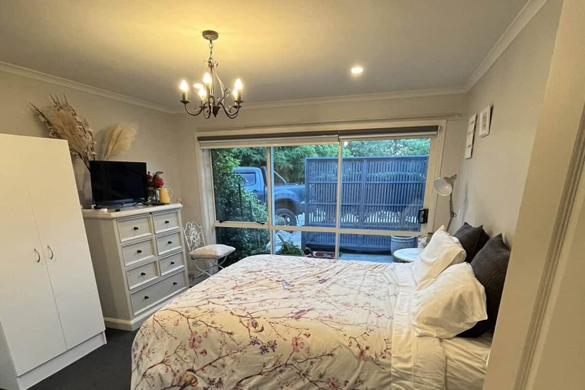 A bedroom with a bed, a dresser, a TV, and a window with a view of a blue truck and a fence.