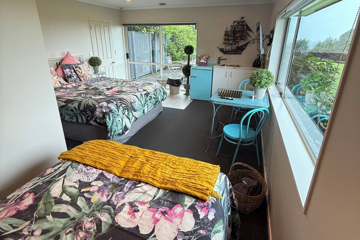 A bedroom with two beds, a small kitchenette, and a window with a view of greenery.