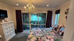 Une chambre à coucher avec un grand lit, un lustre, une commode, un téléviseur et une vue sur l’extérieur par une fenêtre.