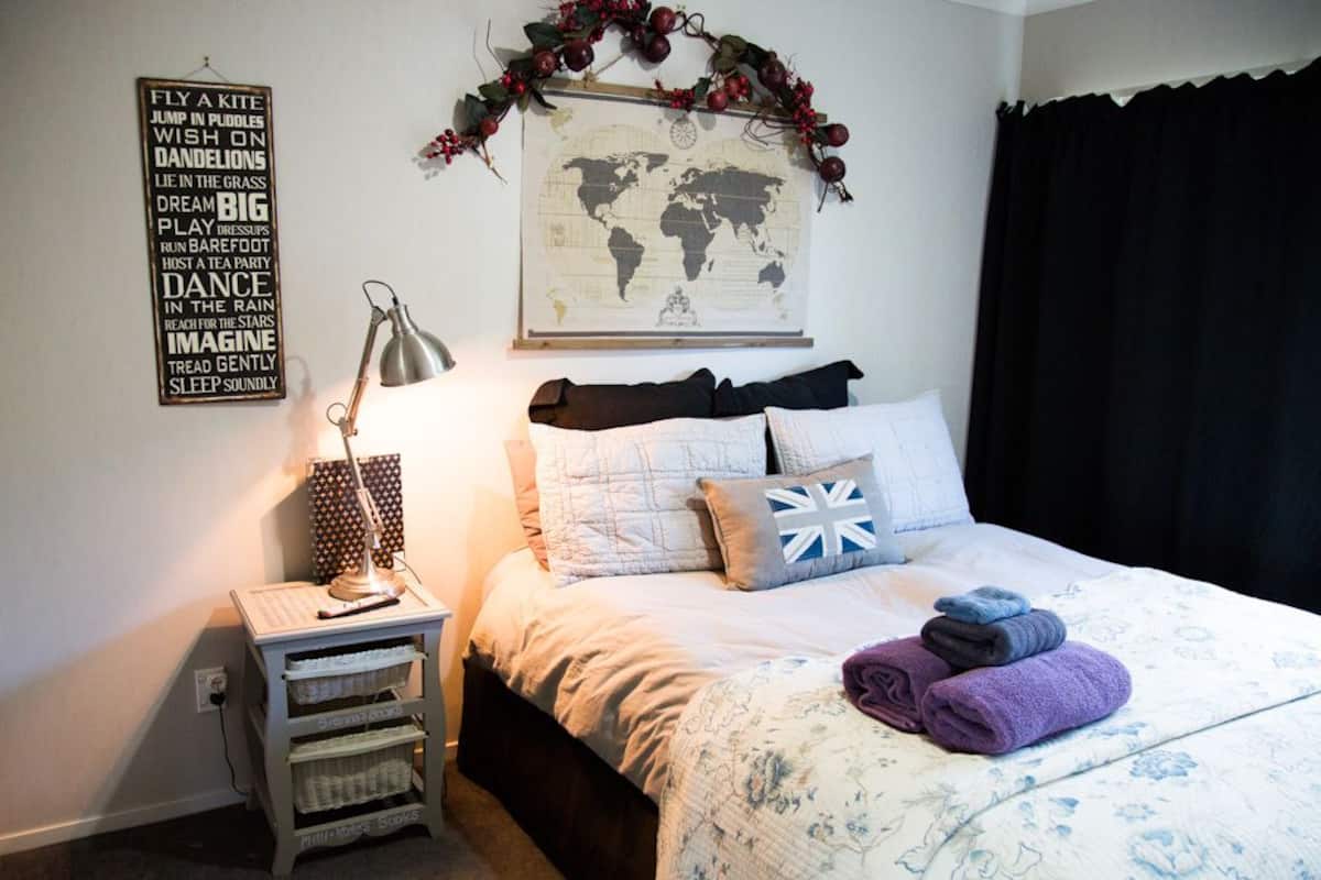 A neatly arranged bedroom with a bed, pillows, a lamp, a world map, and a motivational quote on the wall.