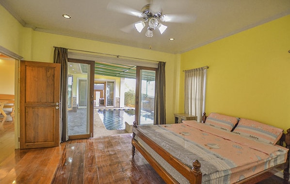 A bedroom with a bed, a wooden door, a ceiling fan, and a view of a pool through a glass door.