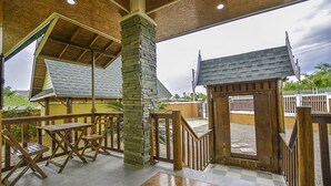 A covered outdoor area with wooden furniture and a stone pillar. - Baan San Rak By Puppap (Cha-am)