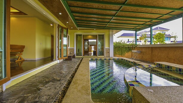An indoor swimming pool with a tiled floor and a wooden bench. - Baan San Rak By Puppap (Cha-am)