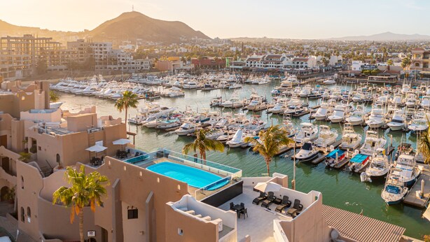 A marina with numerous boats docked, a swimming pool, and a view of the cityscape and mountains in the background. - Studio Suite at Marina Cabo Plaza (Cabo San Lucas)