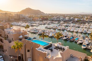 A marina with numerous boats docked, a swimming pool, and a view of the cityscape and mountains in the background. - Studio Suite at Marina Cabo Plaza (Cabo San Lucas)