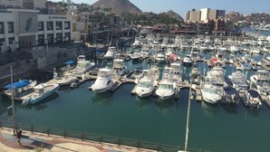 A marina with numerous boats docked, a large building labeled 'Luxury Avenue', and a mountainous backdrop. - Studio Suite at Marina Cabo Plaza (Cabo San Lucas)