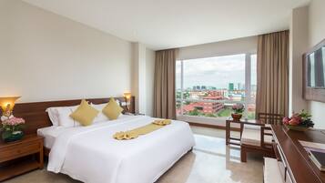 A hotel room with a large bed, a desk, a chair, a TV, and a window with a city view.