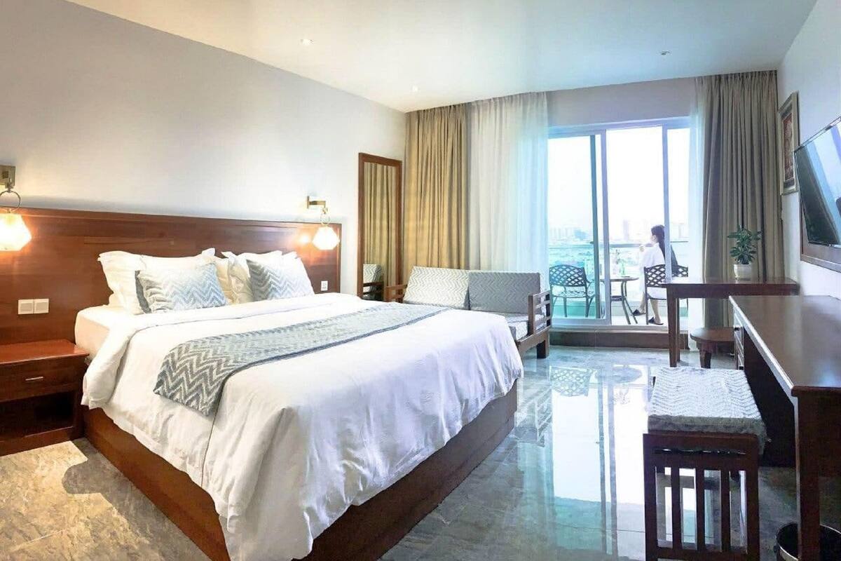 A hotel room with a large bed, a desk, a chair, and a balcony with a view.