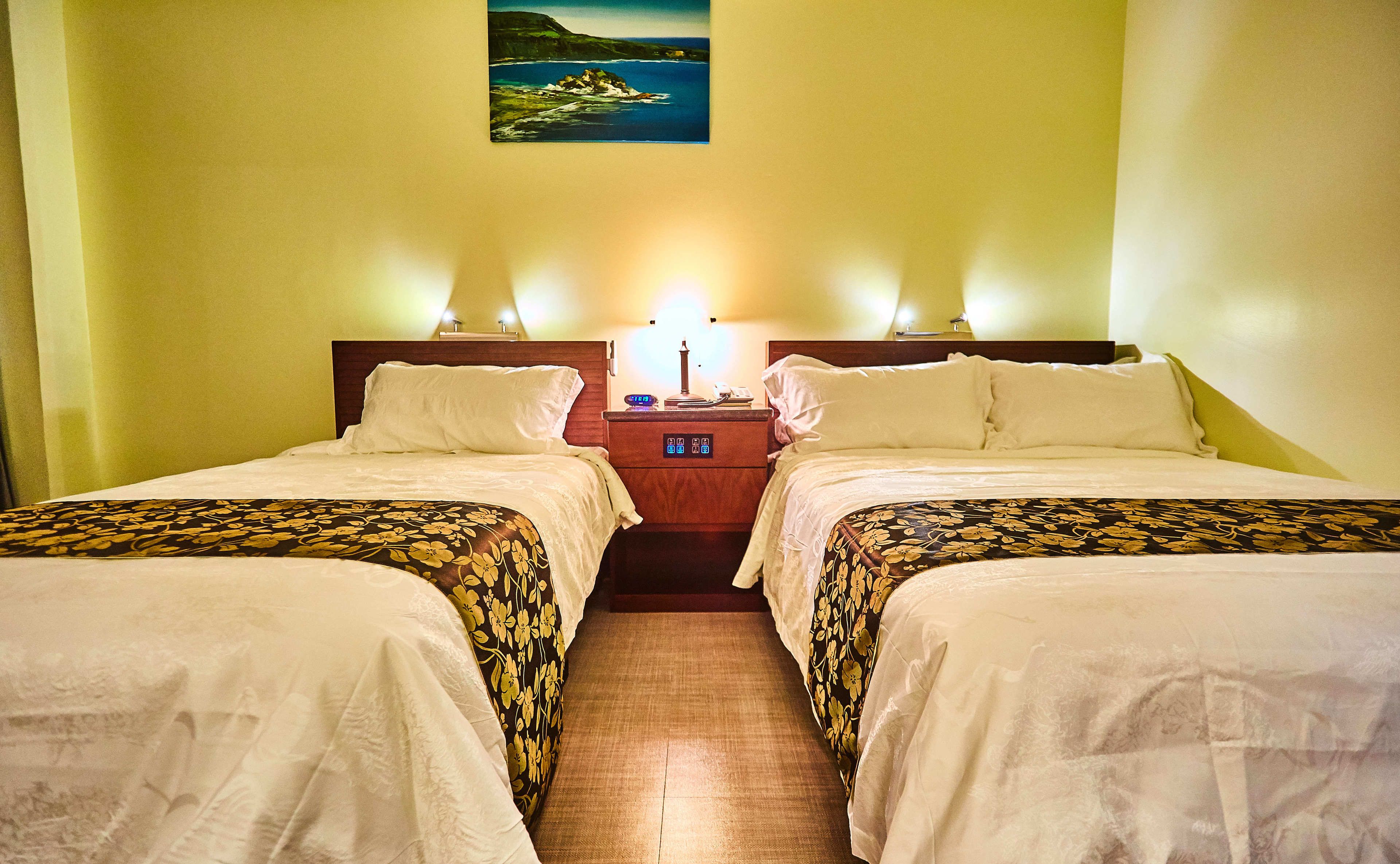 A hotel room with two beds, a nightstand with a lamp, and a painting on the wall.