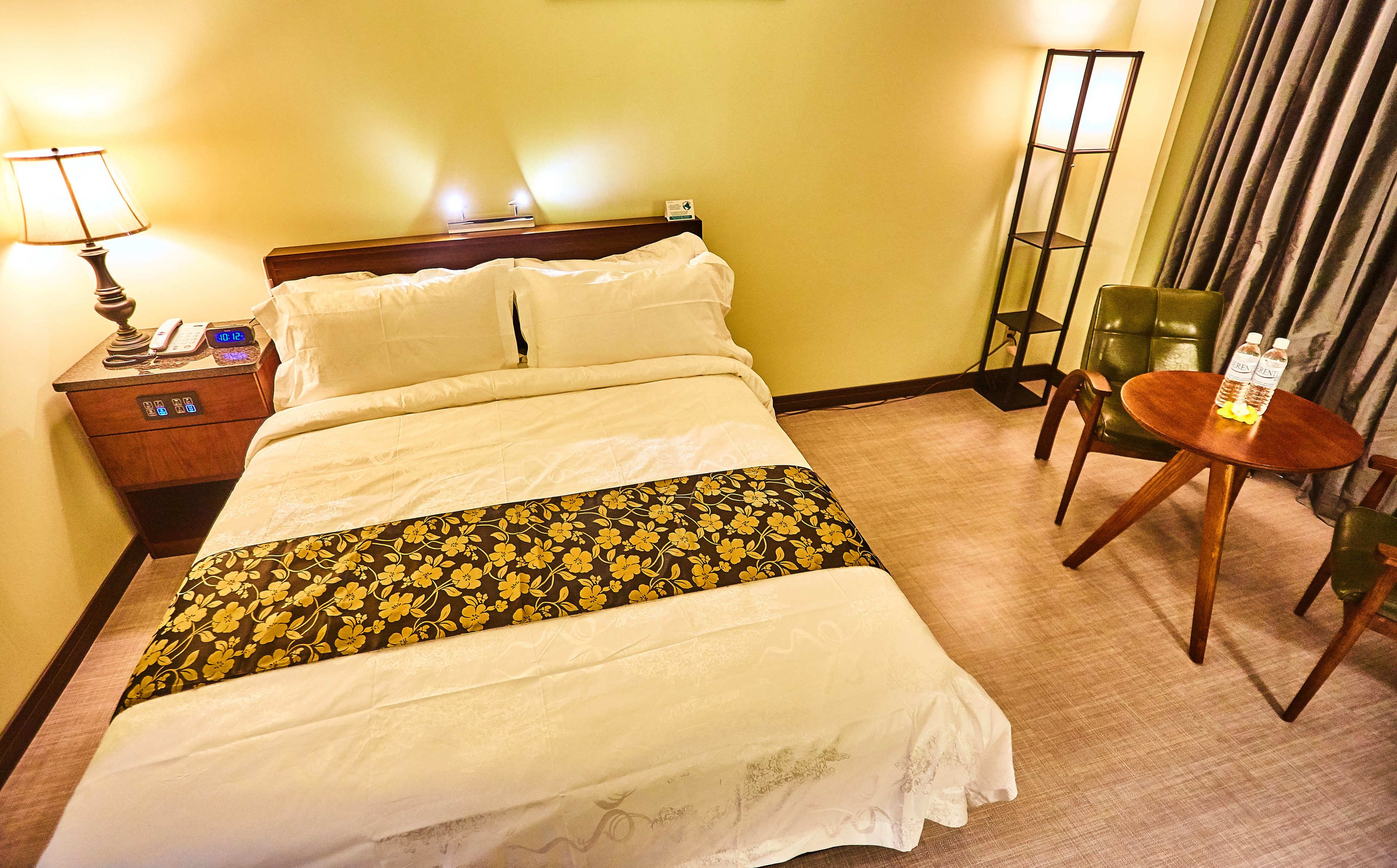Une chambre d’hôtel avec un lit, une table de chevet avec une lampe, une chaise et une petite table sur laquelle sont posées des bouteilles.