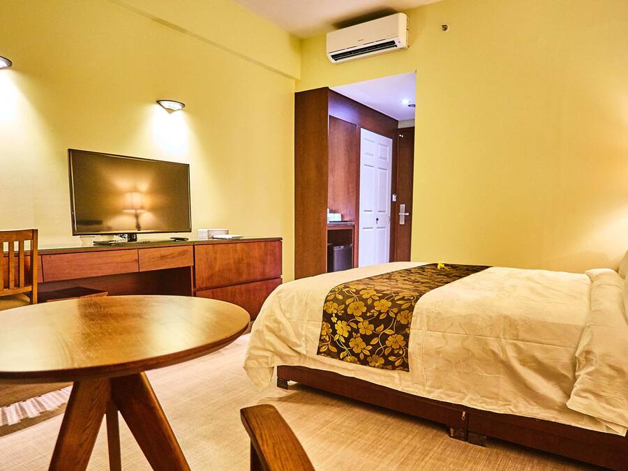 A hotel room with a bed, a desk, a chair, a television, and a lamp.