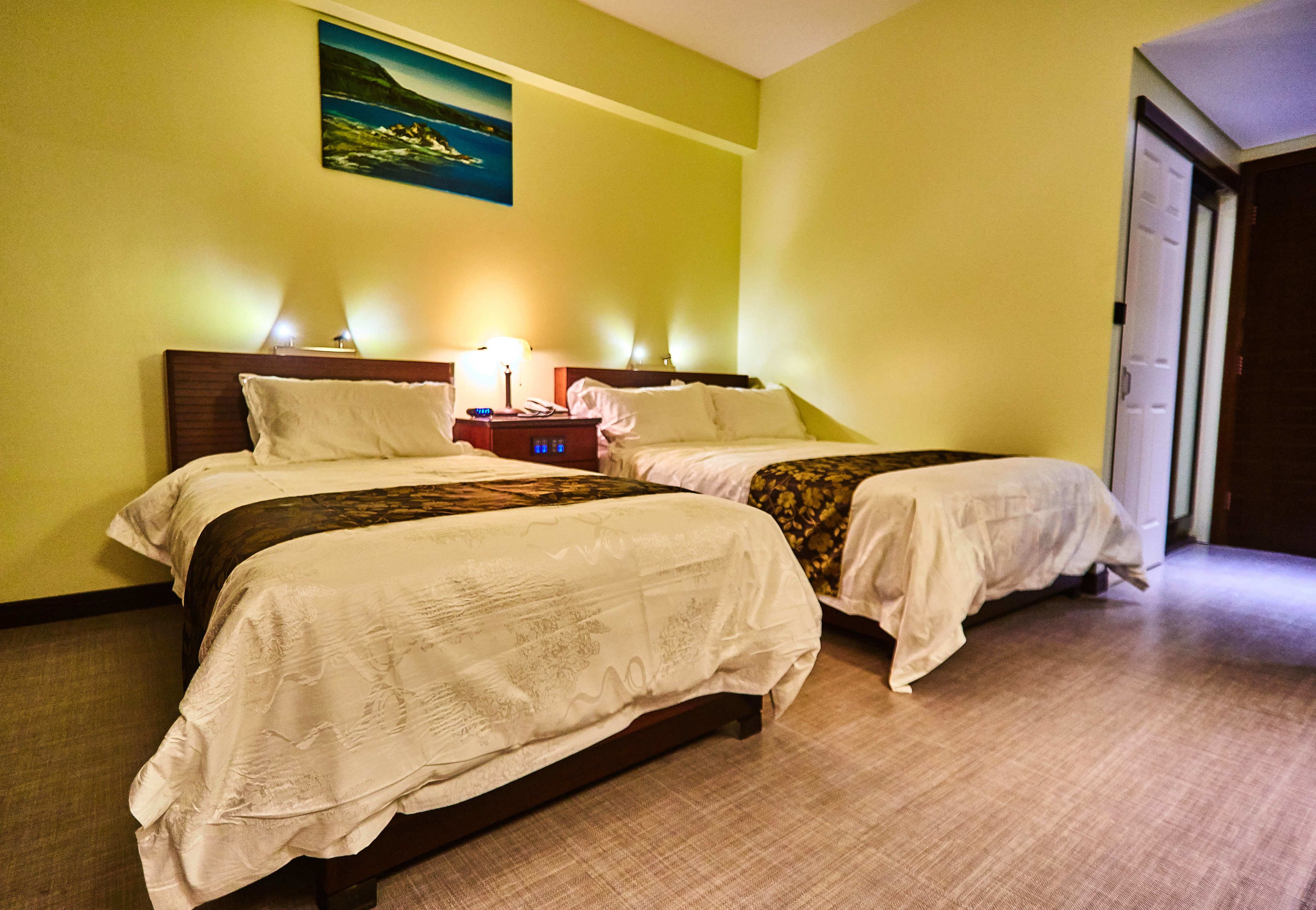 A hotel room with two beds, a nightstand with a lamp, and a painting on the wall.