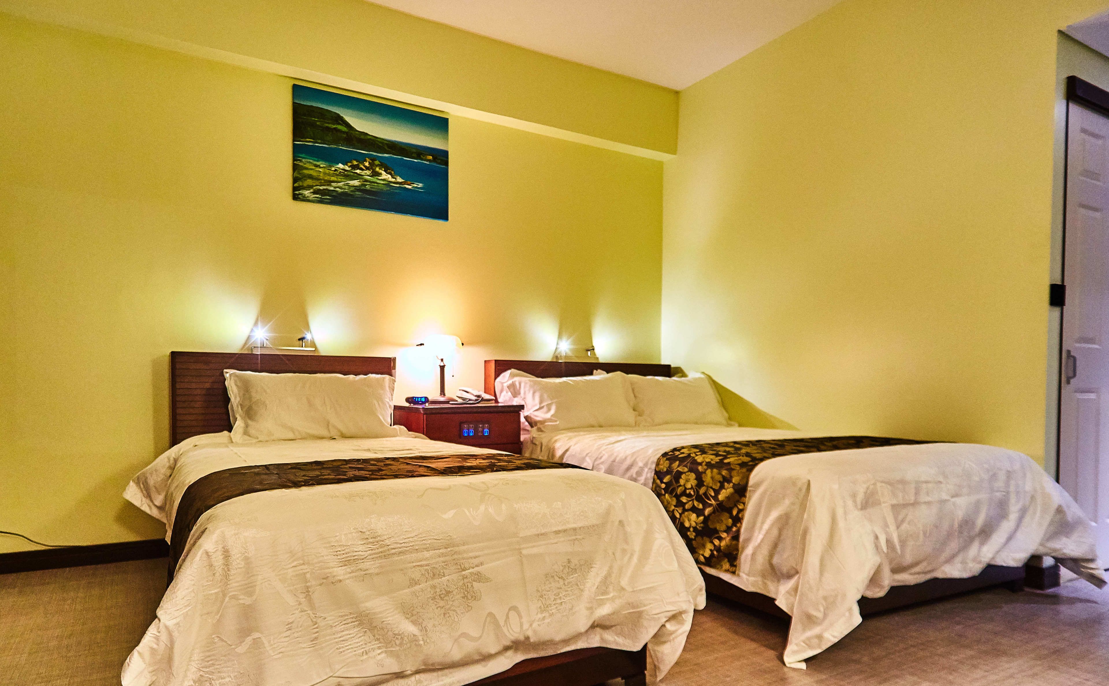 Een hotelkamer met twee bedden, een nachtkastje met een lamp en een schilderij aan de muur.